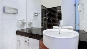 Un baño moderno con un lavamanos grande de color blanco, una mampara de cristal y una zona de ducha con azulejos negros.