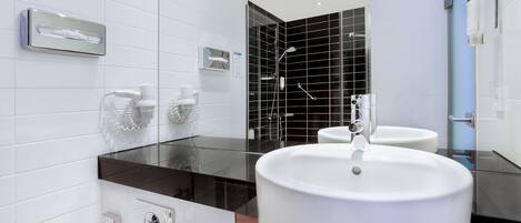 A modern bathroom with a large white sink, a glass partition, and a black-tiled shower area.