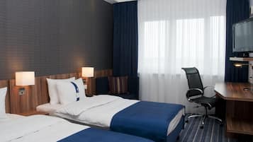 A hotel room with two beds, a desk, a chair, a TV, and a window with curtains.