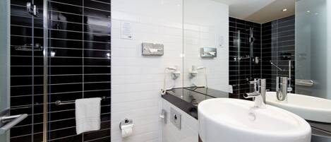 Un baño moderno con cabina de ducha de vidrio, inodoro y lavabo blancos, y un espejo sobre éste.