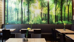 Un restaurante con un mural temático de bosque, mesas de madera y sillas negras.