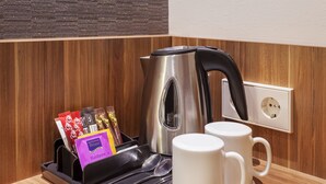 Una zona de cocina con hervidor, tazas de café y una bandeja con cápsulas de café.