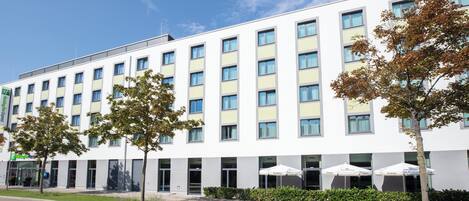 A modern hotel building with multiple floors, large windows, and a well-maintained lawn area.
