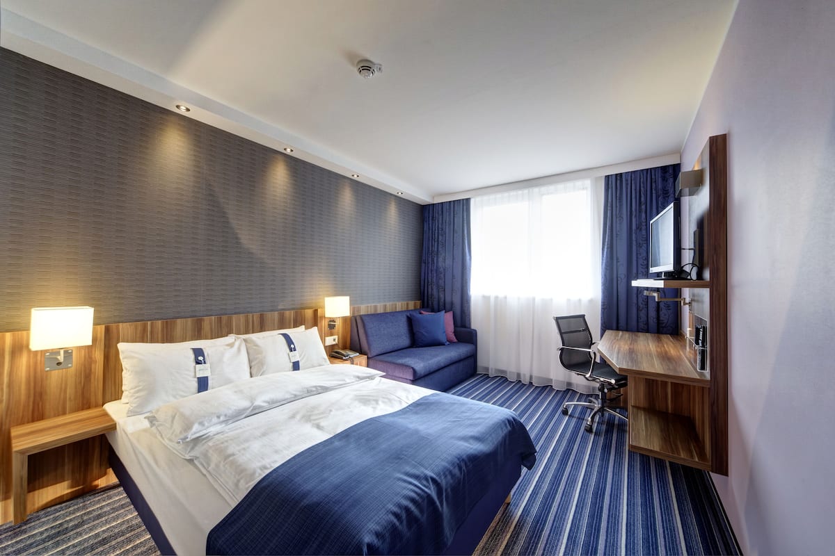 A hotel room with a large bed, a sofa, a desk, and a TV.