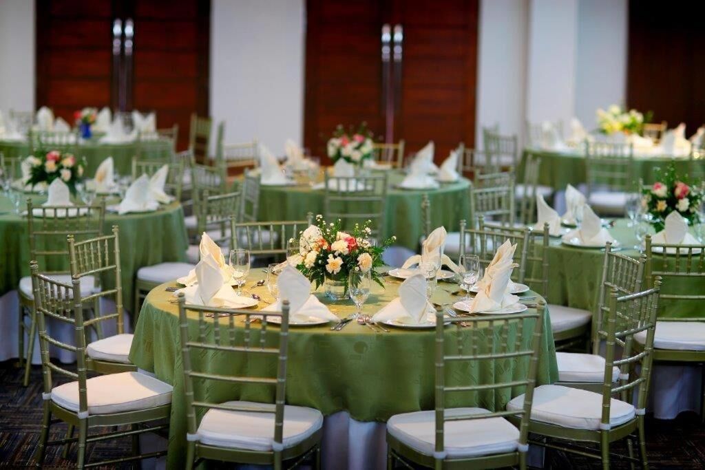 A banquet hall with round tables covered in green tablecloths, white napkins, and floral centerpieces.