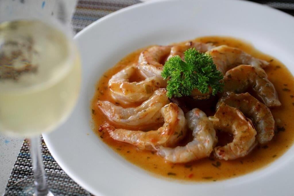 A plate of cooked shrimp with a garnish, accompanied by a glass of white wine.