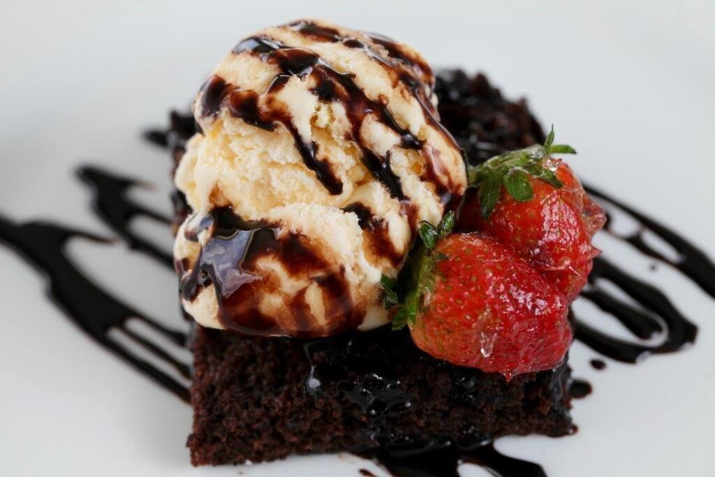 Ein Dessert mit einer Kugel Eis, schokoladiger Soße, einer Erdbeere und einem Stück Kuchen.