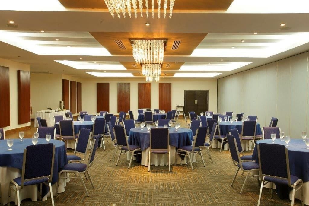 Un salón de conferencias con mesas redondas, manteles azules y sillas a juego.