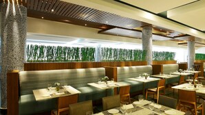 Een restaurant met zitjes en tafels, houten lambrisering en groene planten.