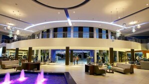 Een ruime lobby met een fontein in het midden, meerdere zithoeken en een gebogen plafond met hangende lampen.