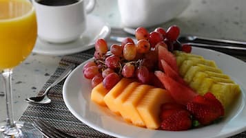Un piatto di frutta con uva, anguria, melone cantalupo e fragole, accompagnato da un bicchiere di succo d'arancia e una tazza di caffè su un tavolo.