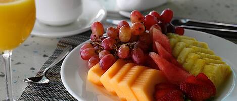 Un plato de fruta que incluye uvas, sandía, melón y fresas, con un vaso de jugo de naranja y una taza de café sobre una mesa.