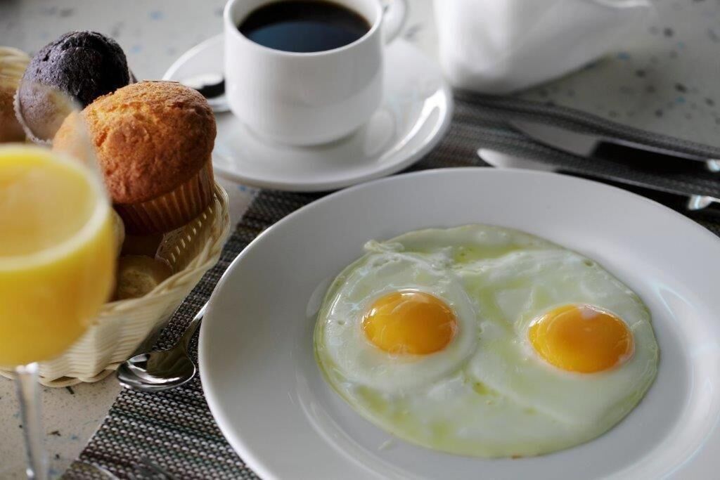 Une table mise pour le petit-déjeuner avec une assiette d’œufs au plat, un panier de muffins, une tasse de café et un verre de jus d’orange.