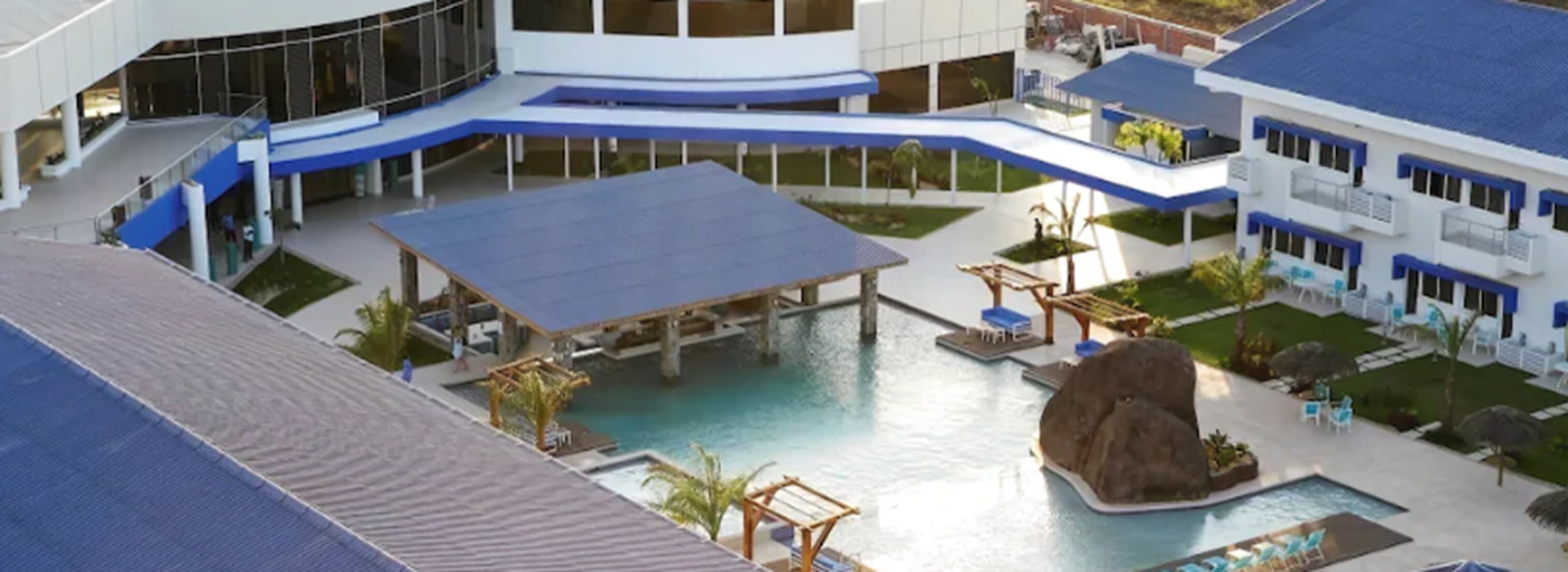A hotel with a swimming pool, covered outdoor seating, and a large rock feature.