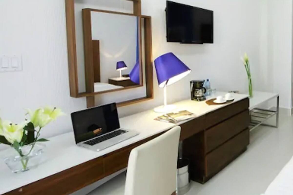 A hotel room with a bed, a desk with a laptop, a TV, and a framed picture on the wall.