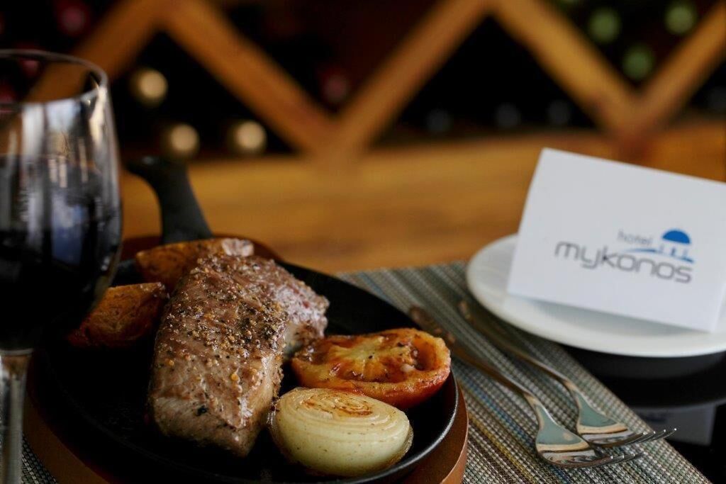 A plate with grilled meat, roasted potatoes, and a grilled tomato, accompanied by a glass of red wine.