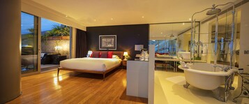 A modern bedroom with a large bed, a glass-enclosed bathroom with a freestanding bathtub, and a view of the outdoors.