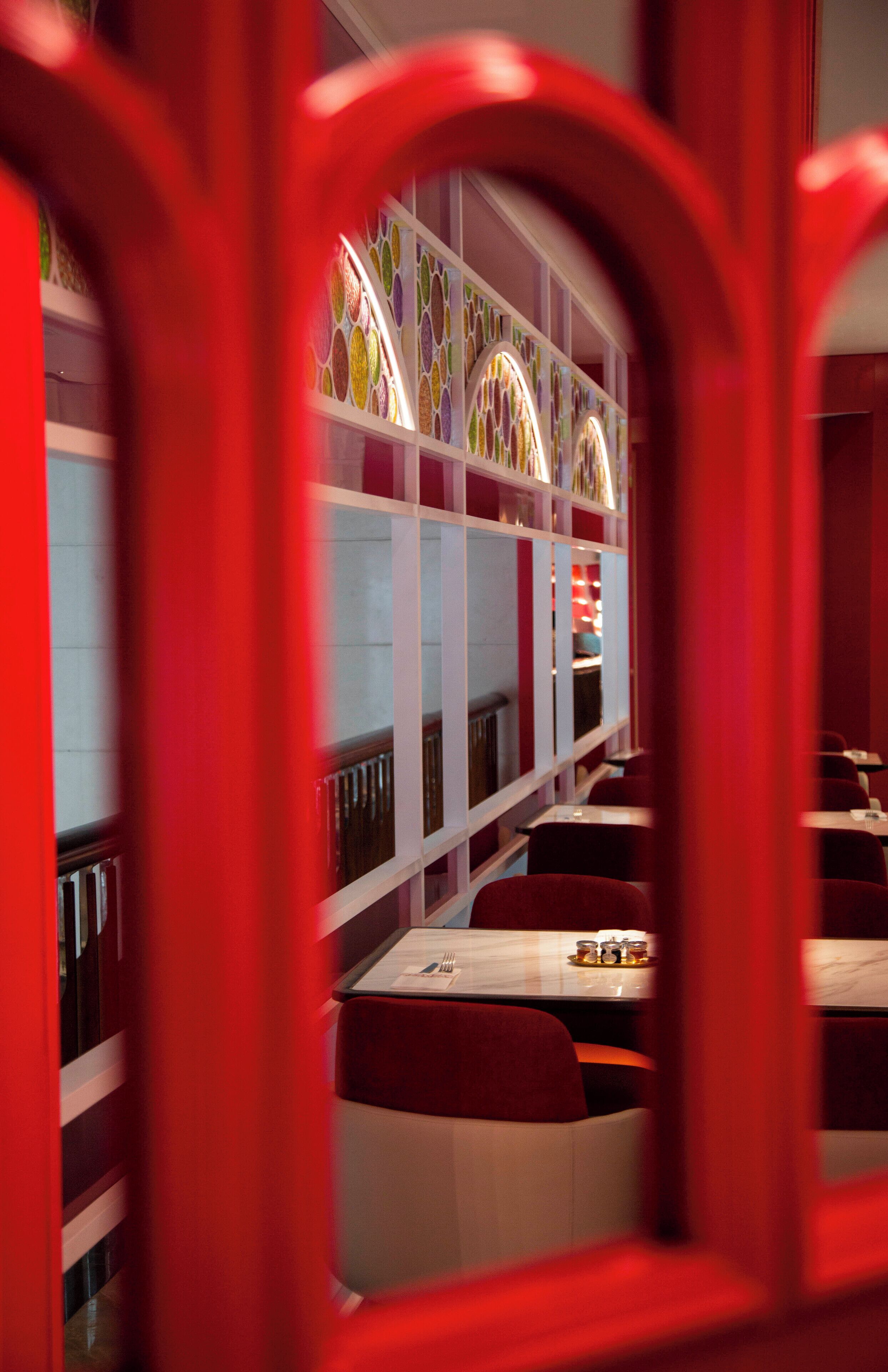 A restaurant with a red and white color scheme, featuring a long counter with seating and a decorative glass wall in the background.
