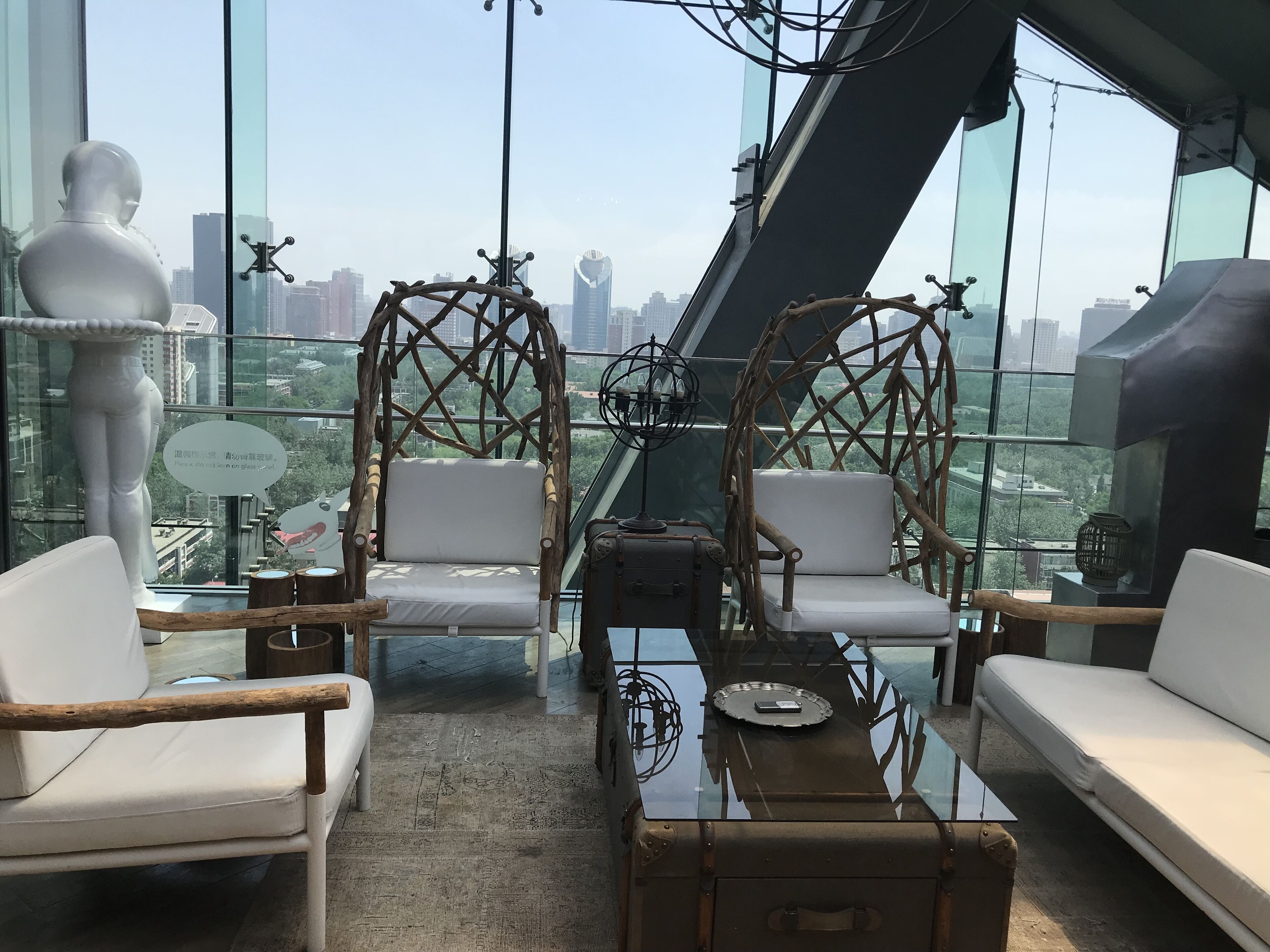 Habitación en un rascacielos con vista a la ciudad, que incluye dos sillones blancos acolchados, una mesa de centro de cristal y un globo decorativo.