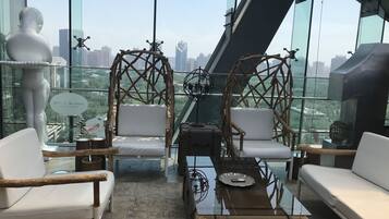 Habitación en un rascacielos con vista a la ciudad, que incluye dos sillones blancos acolchados, una mesa de centro de cristal y un globo decorativo.