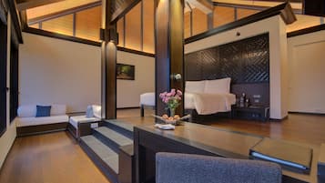A modern hotel room with a bed, a seating area with a sofa and armchair, a small table with a vase of flowers, and a desk with a laptop.