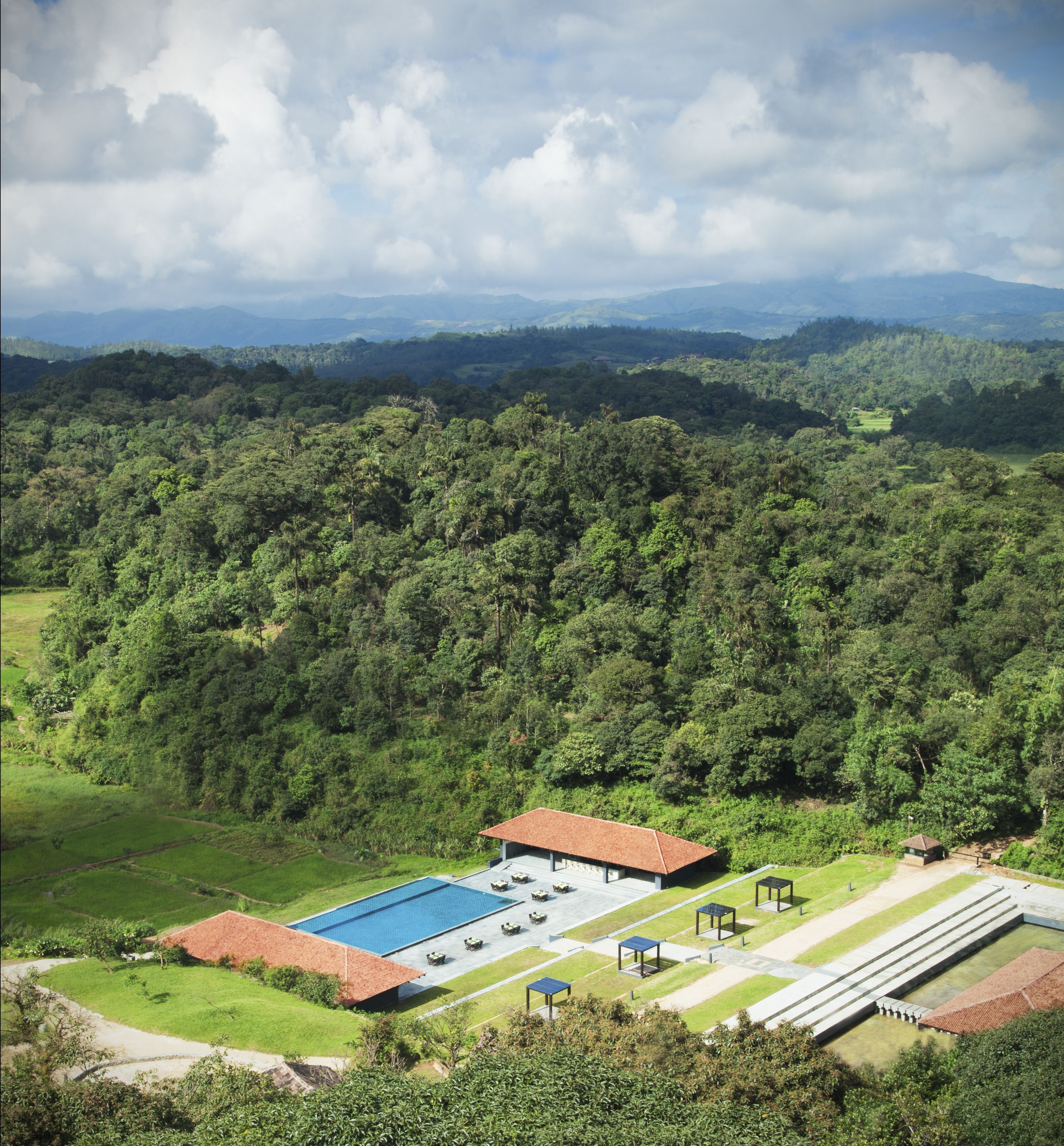 A resort with a swimming pool, outdoor seating, and a view of the surrounding forest and mountains.