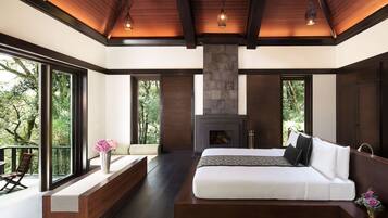 A modern bedroom with a large bed, a stone fireplace, and large windows offering a view of the outdoors.
