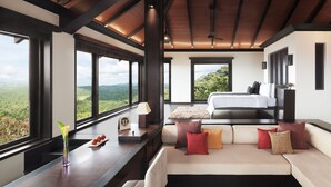 Quarto com cama grande, sofá e vista para o exterior.