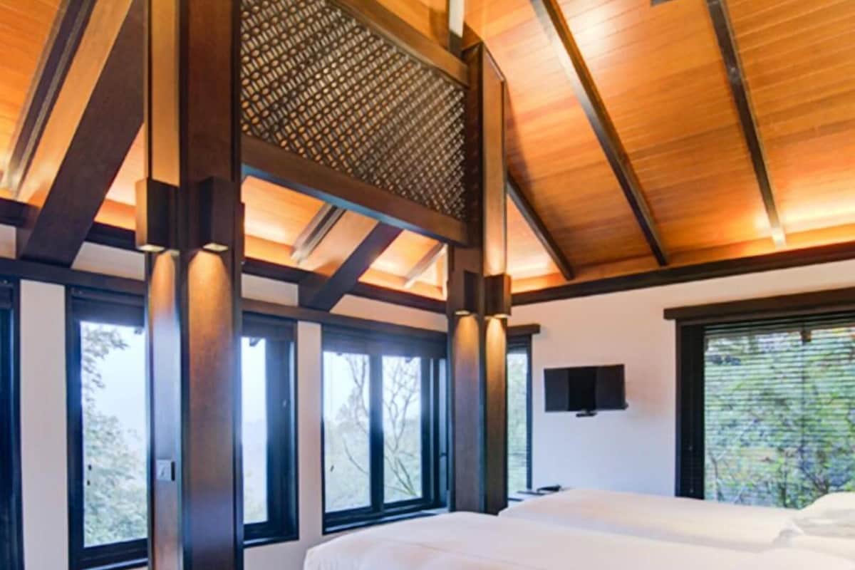 Een moderne slaapkamer met twee bedden, grote ramen en een houten plafond.