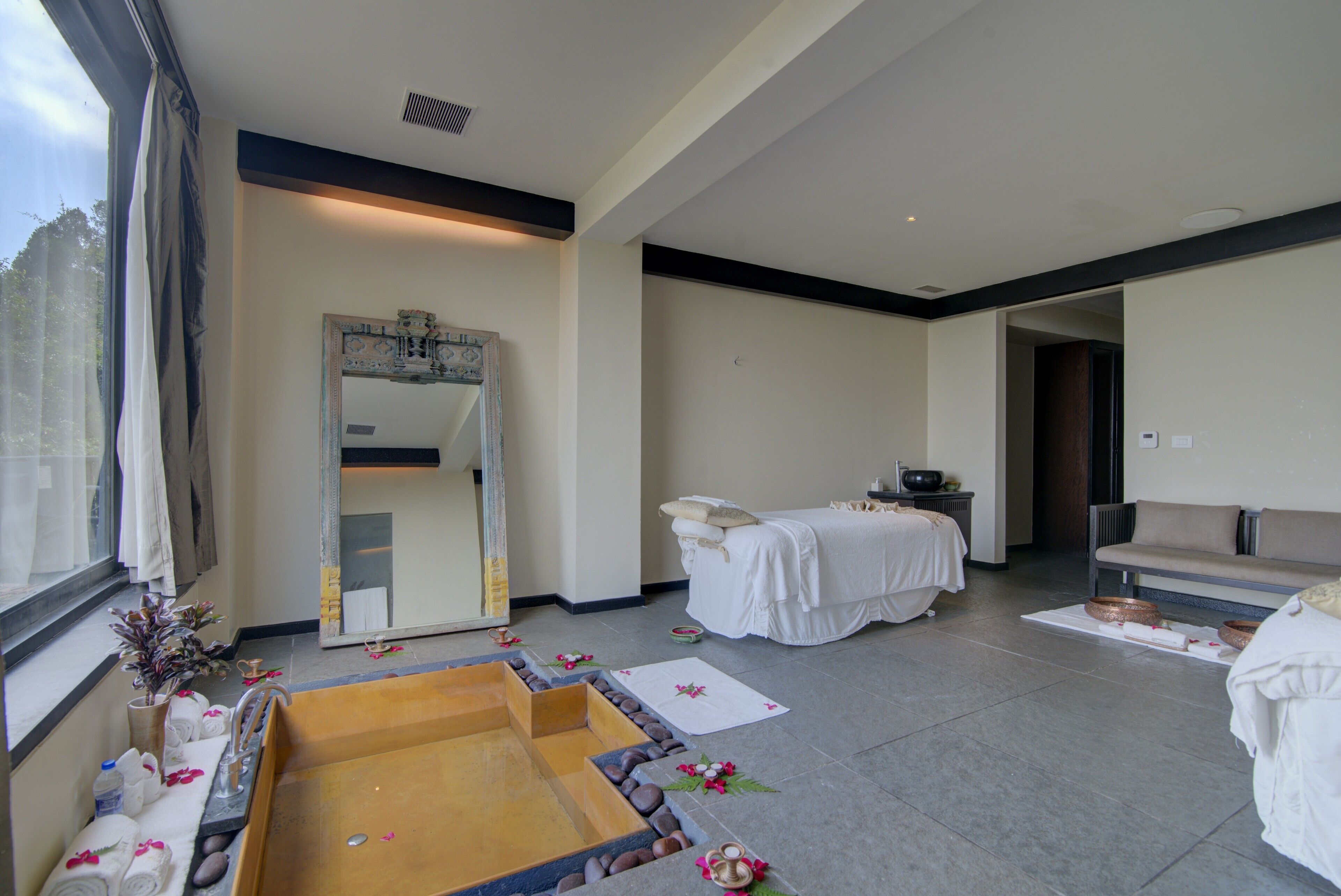 A modern spa room with a large mirror, a massage table, and a stone bath area.