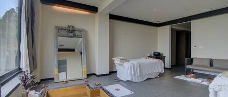 A modern spa room with a large mirror, a massage table, and a stone bath area.