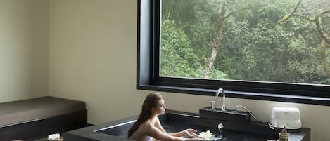Un baño moderno con una bañera grande, un banco y una ventana con vistas a un bosque.