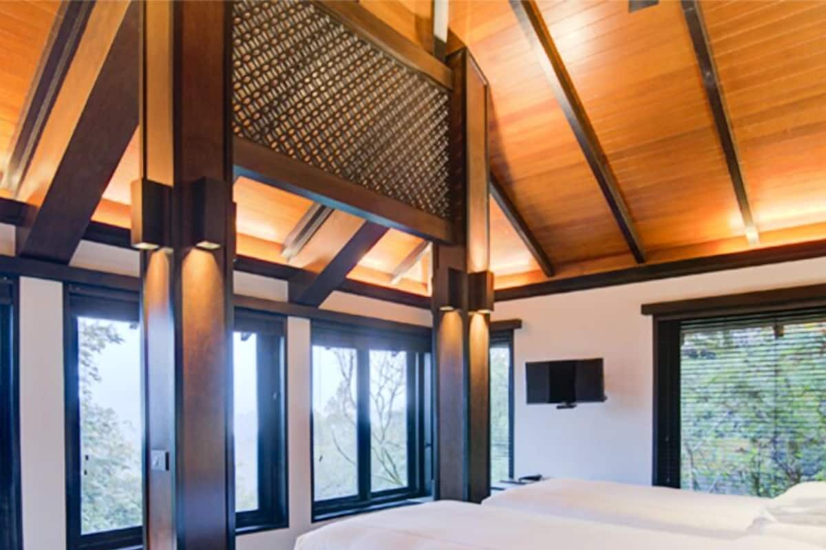 A modern hotel room with two beds, large windows, and a wooden ceiling.