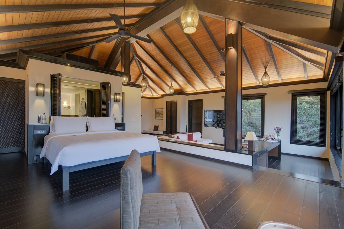 A spacious bedroom with a large bed, a sitting area, a vanity, and a television.