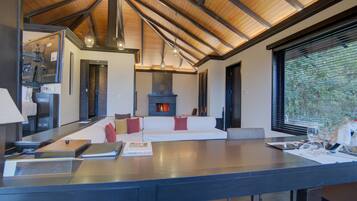 A modern kitchen with a large island, a seating area with a fireplace, and a view through a window.