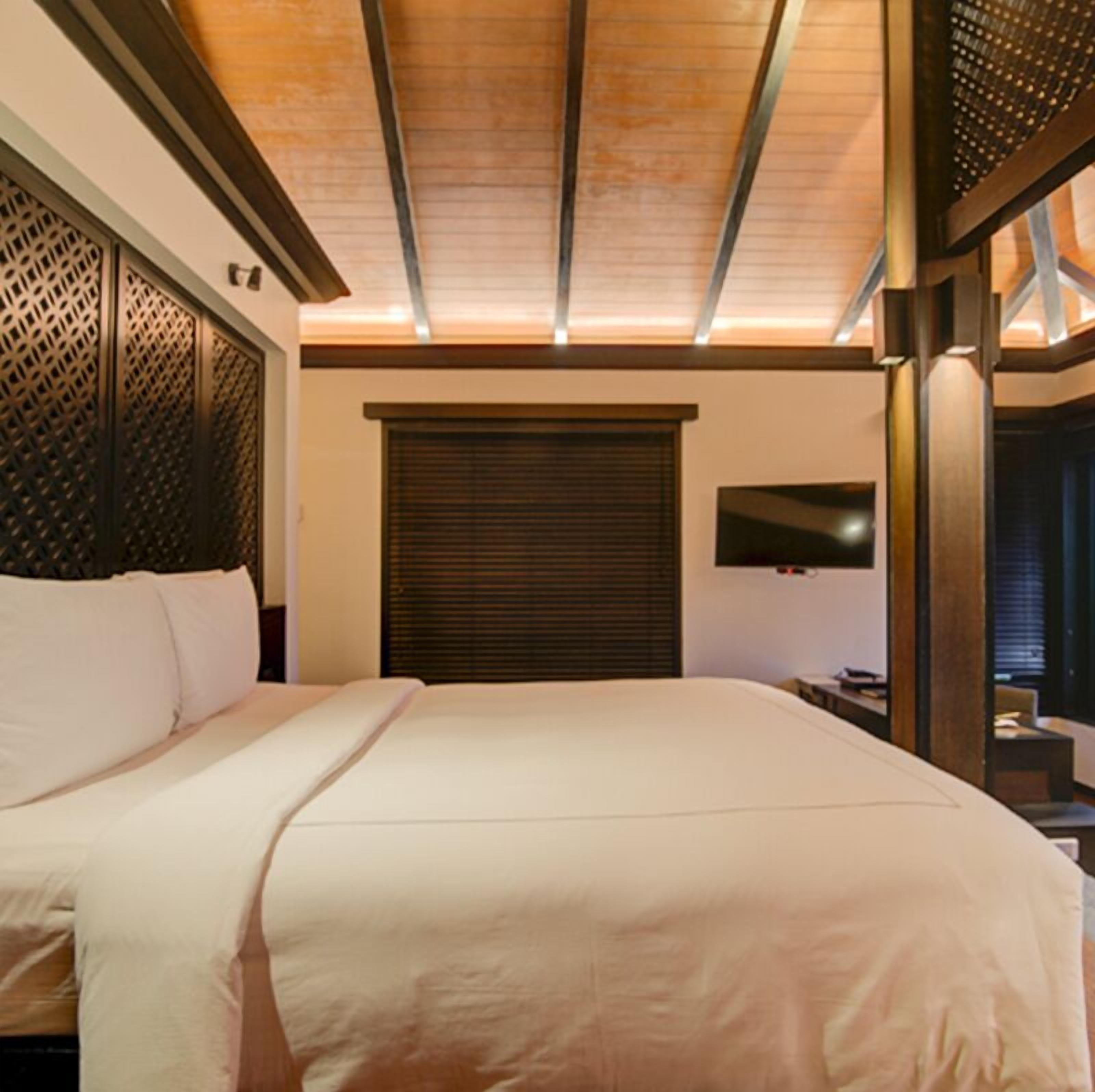A hotel room with a large bed, a TV mounted on the wall, and a wooden ceiling.