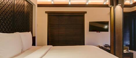 A hotel room with a large bed, a TV mounted on the wall, and a wooden ceiling.