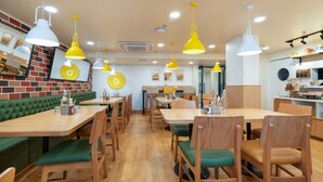 A restaurant interior with multiple dining tables and booths, yellow pendant lighting, and a brick wall with artwork. - Tulip Inn Ahmedabad (Ahmedabad)