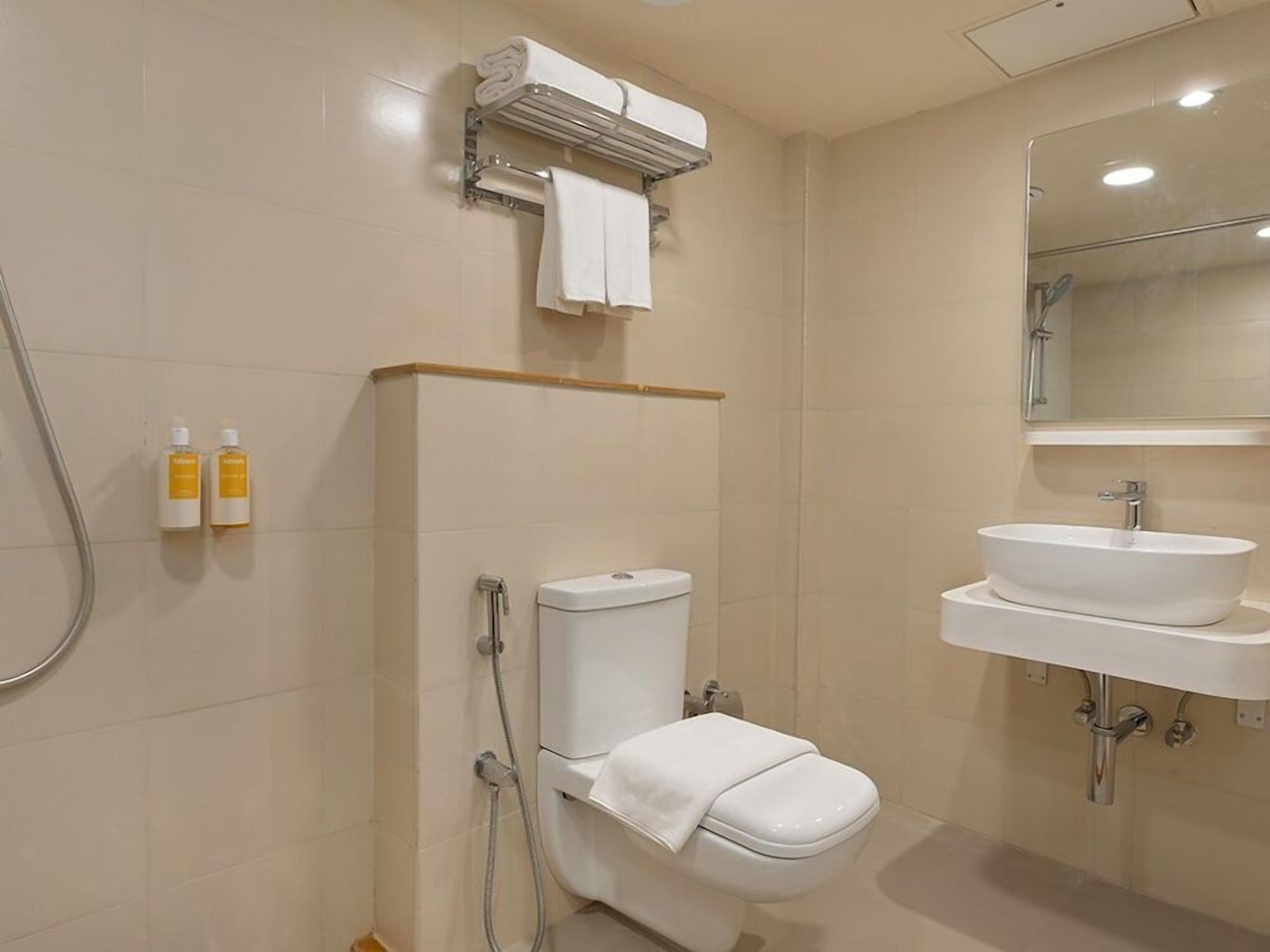 A bathroom with a toilet, a sink, and a shower. There are two bottles of toiletries on the wall.