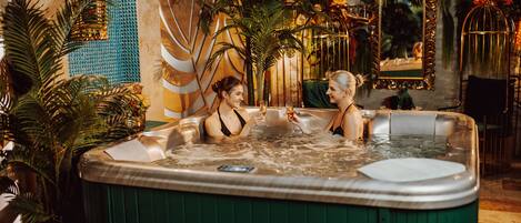 A hot tub with two people sitting inside, surrounded by lush plants and ornate decorations.