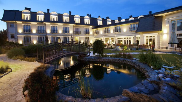 A large, multi-story building with a courtyard featuring a pond, stone pathway, and a bridge. - Rezydencja Luxury Hotel & Wellness (Piekary Slaskie)