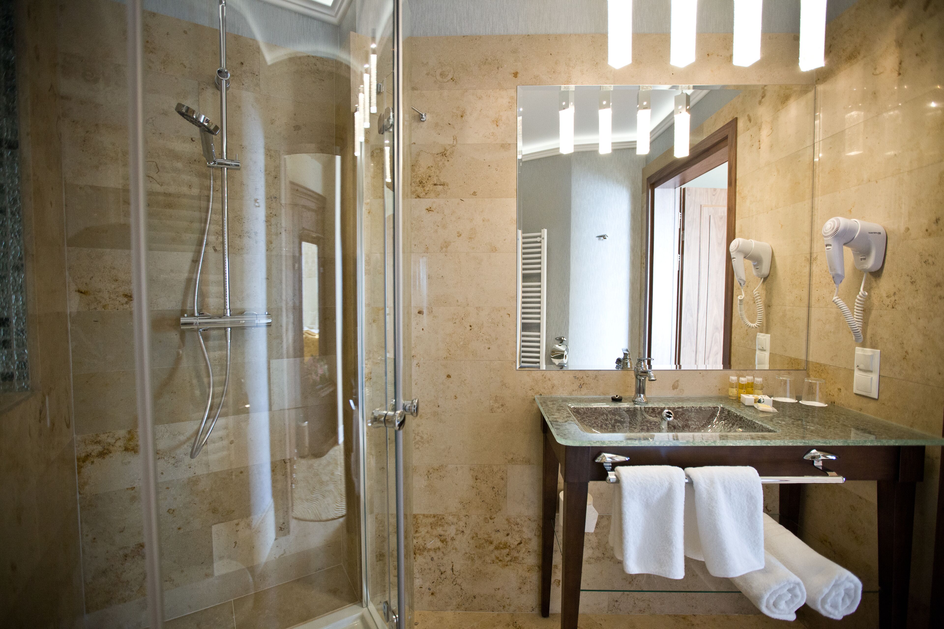 Un baño moderno con ducha envuelta en vidrio, lavabo de vidrio y un espejo grande.