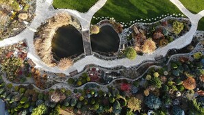 An aerial view of a landscaped garden with two ponds, a winding pathway, and a seating area with tables and chairs. - Rezydencja Luxury Hotel & Wellness (Piekary Slaskie)