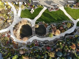 An aerial view of a landscaped garden with two ponds, a winding pathway, and a seating area with tables and chairs.