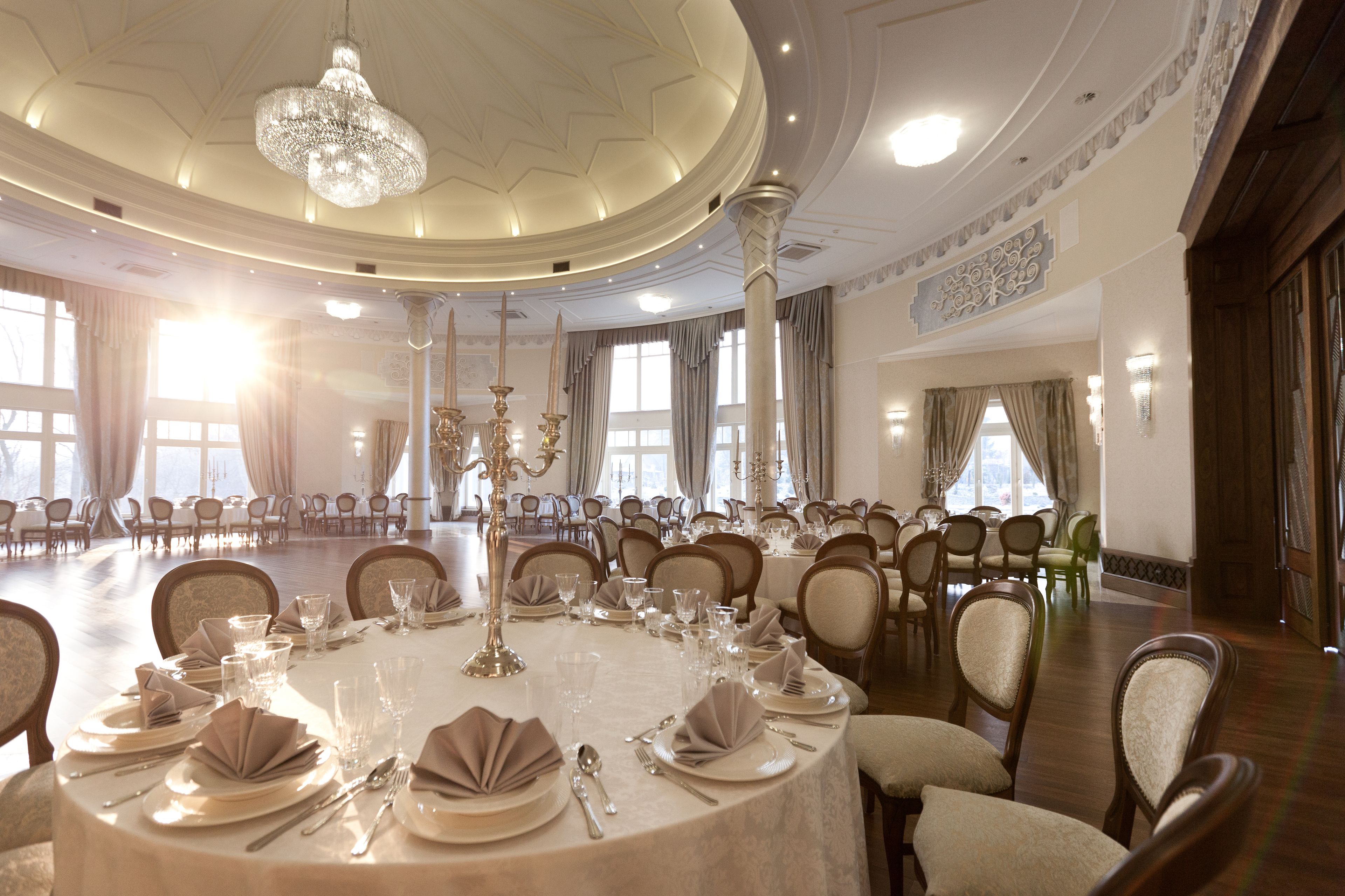 Un amplio salón de banquetes con mesas redondas dispuestas para comer, candelabros y un techo alto.