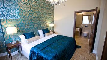 Une chambre d’hôtel avec un grand lit, deux tables de chevet, un lustre et un miroir qui reflète la salle de bain.