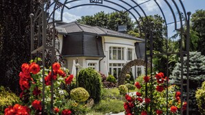 A house with a garden pathway leading to the entrance, surrounded by lush greenery and red flowers. - Rezydencja Luxury Hotel & Wellness (Piekary Slaskie)