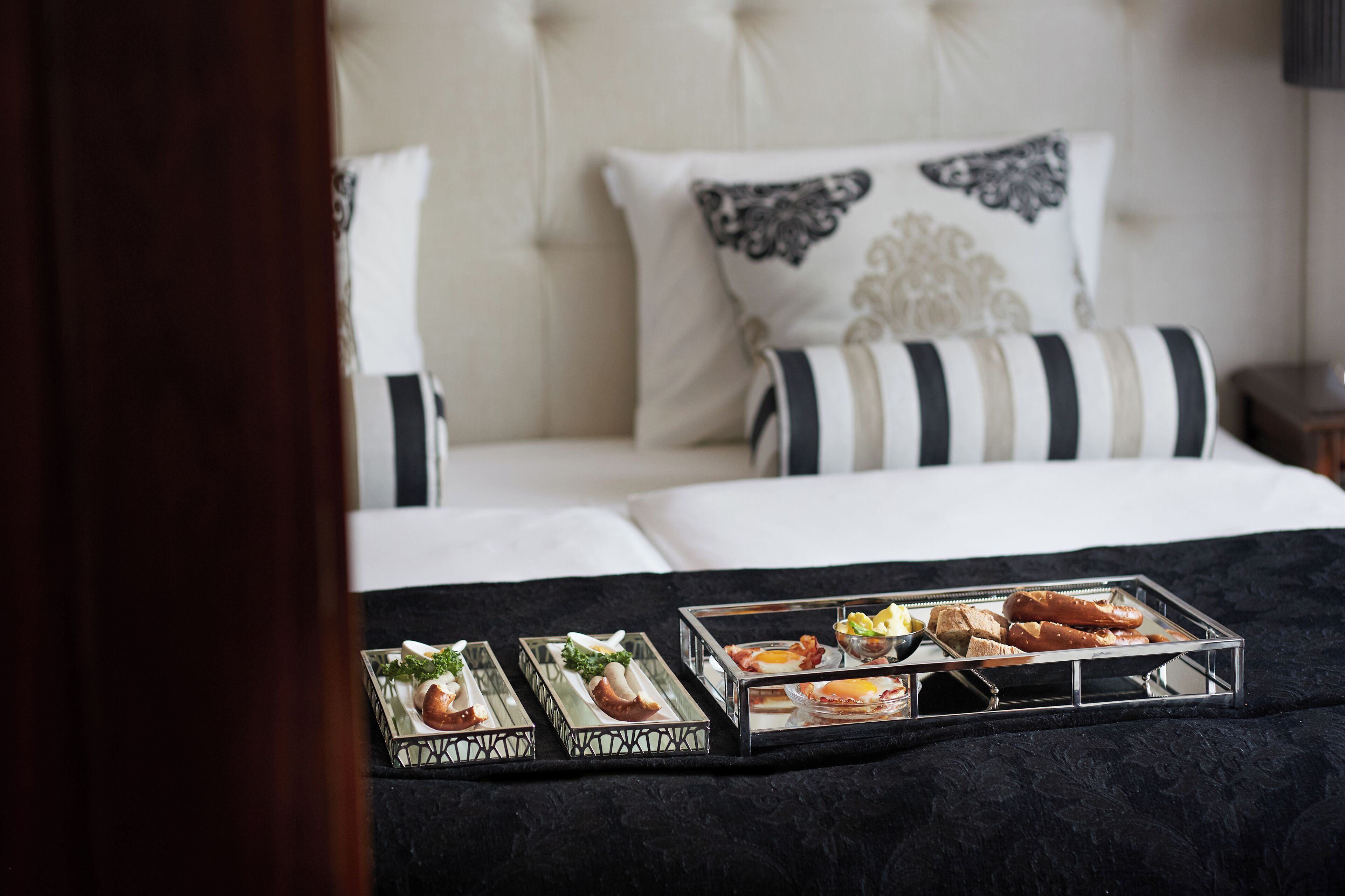 A neatly made bed with a black and white striped pillow, a tufted headboard, and a tray of breakfast items on the bed.