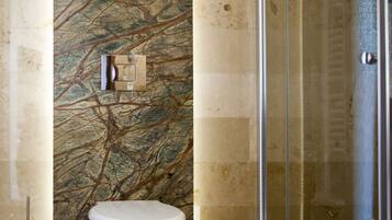 Un baño moderno con pared de mármol, inodoro y cabina de ducha de vidrio.