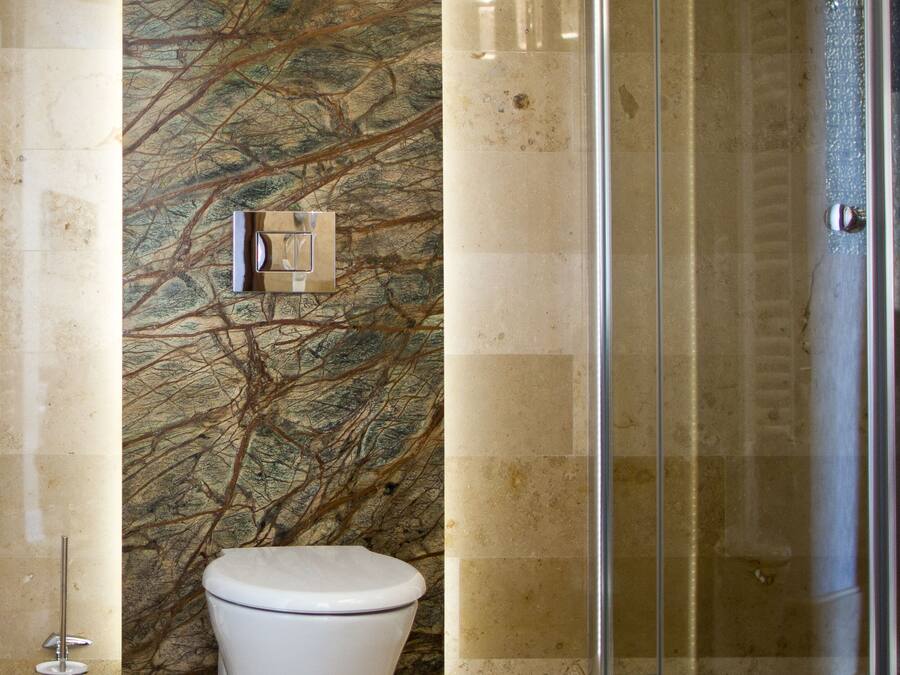 Un baño moderno con pared de mármol, inodoro y cabina de ducha de vidrio.